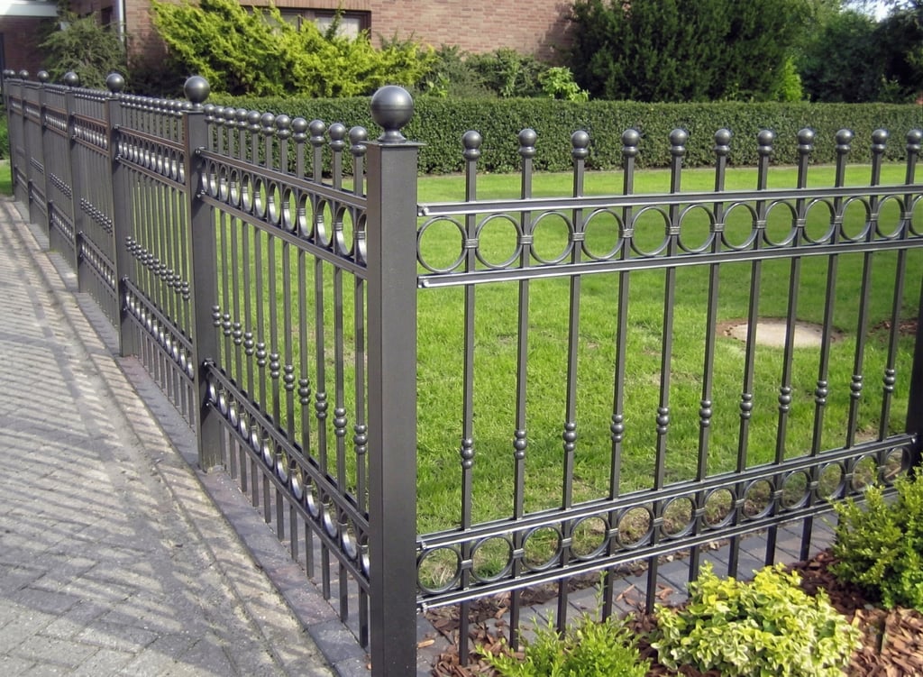 Black ornamental wrought iron fence with decorative circles and finials surrounding a green garden lawn.