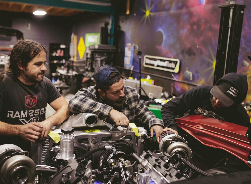 Three mechanics working on a high-performance car engine with turbochargers in an automotive garage.
