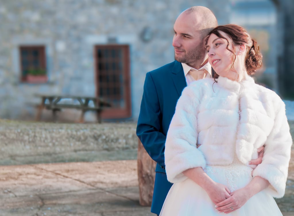 Une mariée vêtue d'un manteau de fourrure blanche et un marié en costume bleu posent