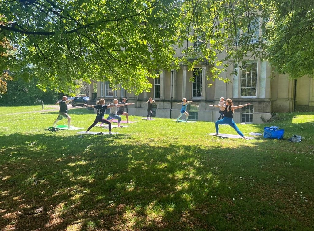 Outdoor yoga class practising poses on grass in a park.