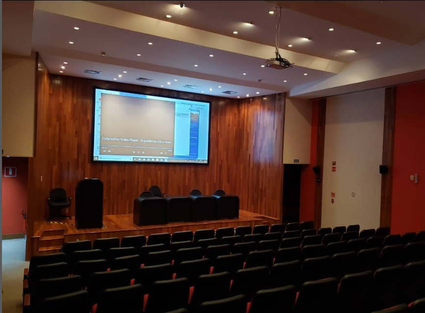 Tela elétrica e projetor em auditório grande com cadeiras pretas