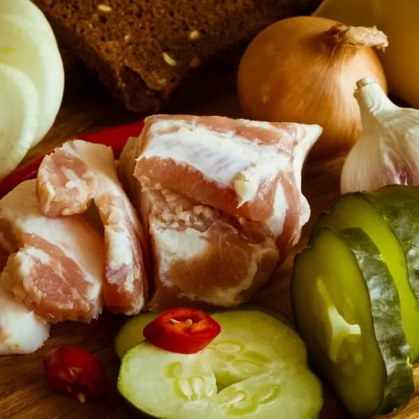 Frische Zutaten für Schmorgurken mit Speck: Salatgurken, Speckwürfel, Zwiebeln und frischer Dill auf