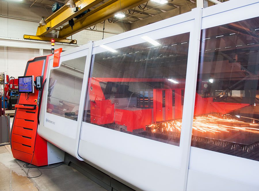 Industrial CNC laser cutting machine in a factory workshop creating sparks during metal fabrication.