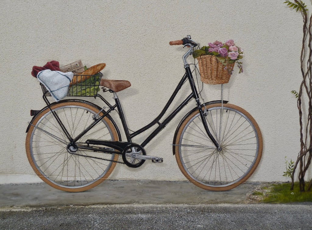 Un vélo peint en trompe-l'oeil sur une façade. Ses paniers emplient de fleurs et autres courses.