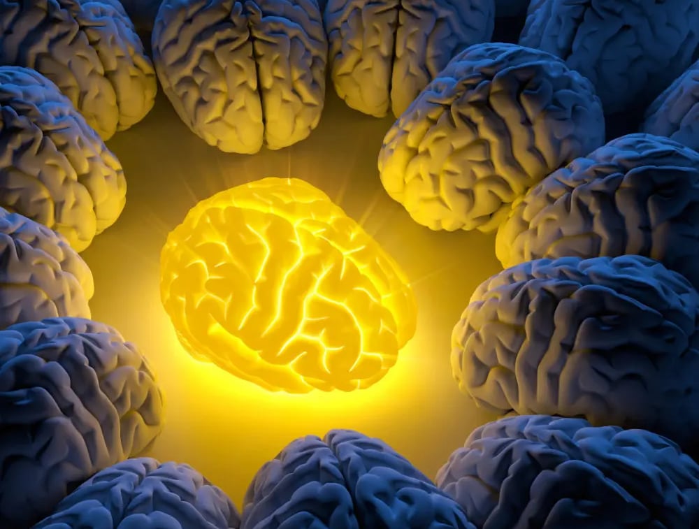 A yellow glowing brain in the middle of darker brains, illuminating them.