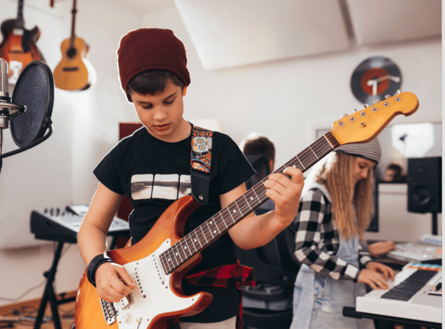 young boy playing guitar and young girl working sound tech in background