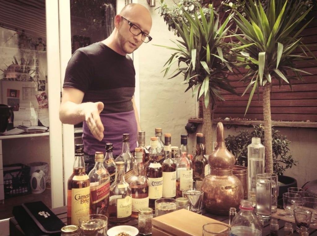 a man in a black shirt is standing in front of a table with bottles of whisky