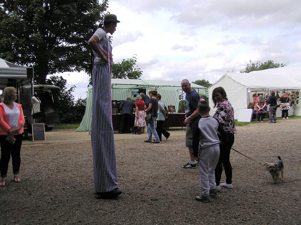 A circus entertainer on stilts wearing striped trousers performs for a crowd at an outdoor community festival.