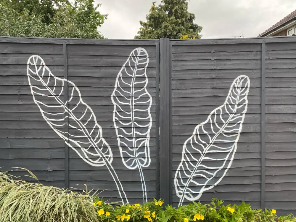 Modern graphic mural of three large tropical leaves on grey yard fence with flowers, by House of Lyr