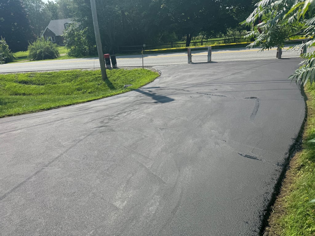 Freshly paved blacktop residential driveway leading to a rural road with yellow caution tape.