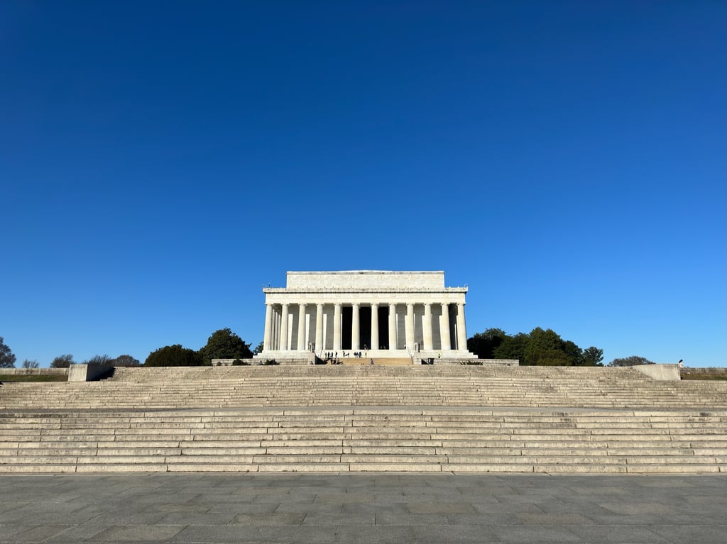 The Lincoln Memorial, a large white building with columns in front of of a blue sky