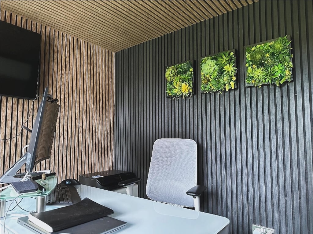 Modern home office featuring wood slat wall panels, a white desk, and framed artificial succulent wall art.