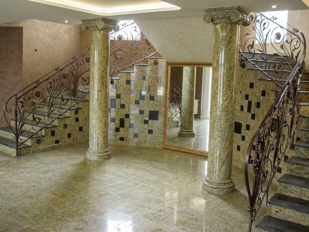 Luxury interior with marble columns, granite flooring, and an ornate wrought iron staircase.