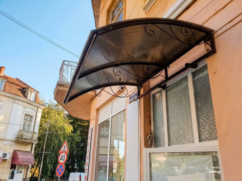 Curved bronze polycarbonate door awning with decorative wrought iron brackets on a city building.