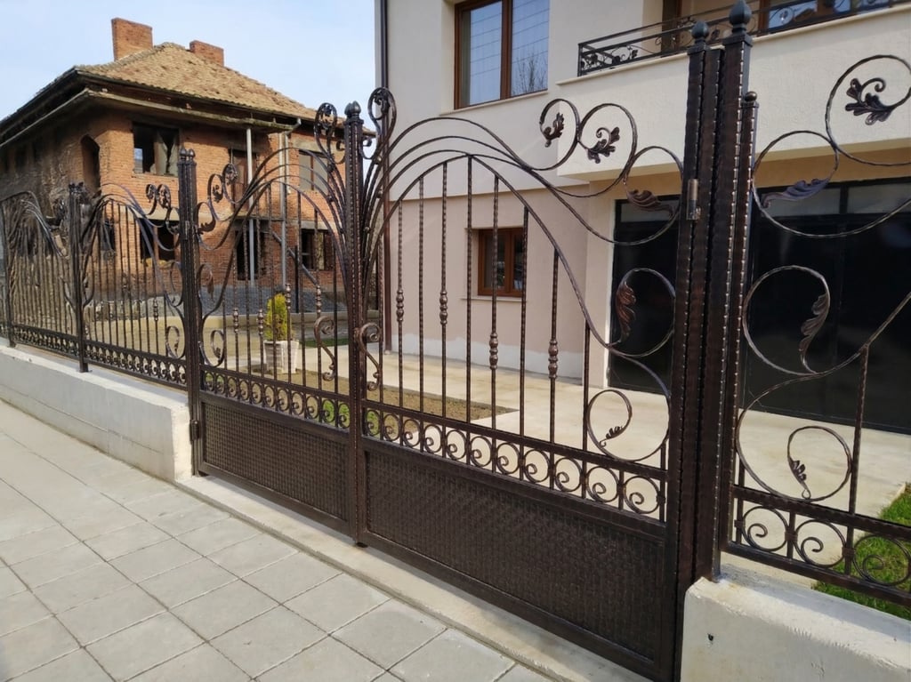 Elegant dark brown wrought iron driveway gate and matching fence with ornate scrollwork details.