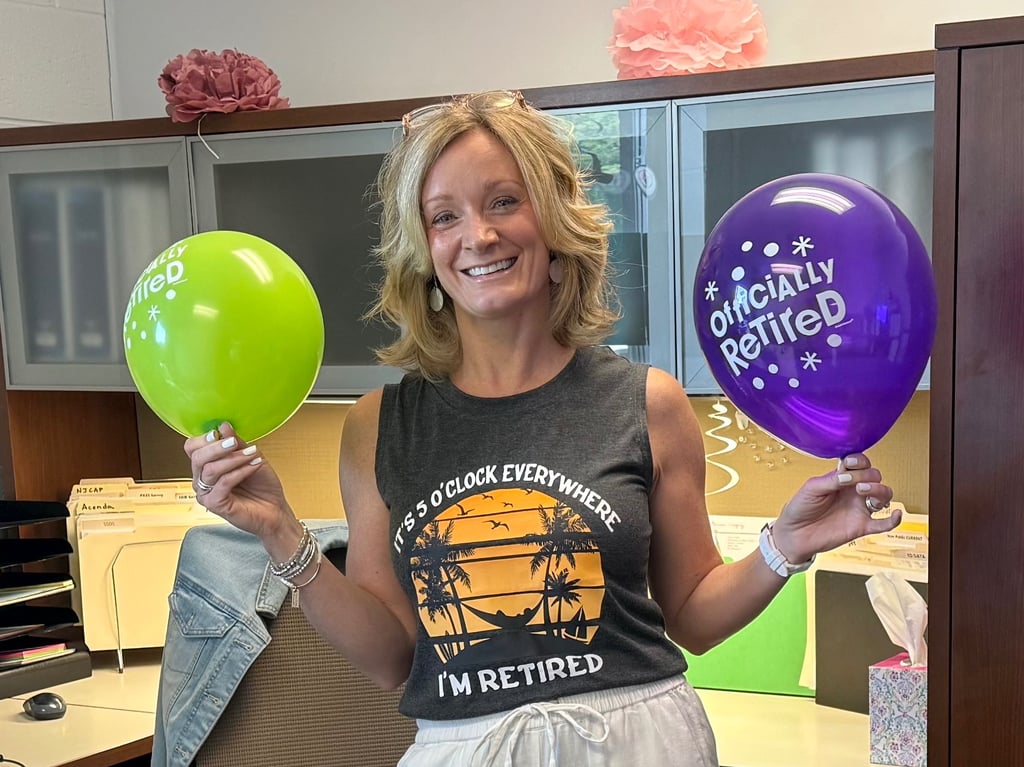 Smiling woman holding retirement balloons on her last day of work, celebrating retirement