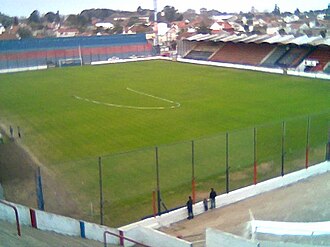 Estádio do Tigre visto das arquibancadas, com campo iluminado e torcida presente durante partida.