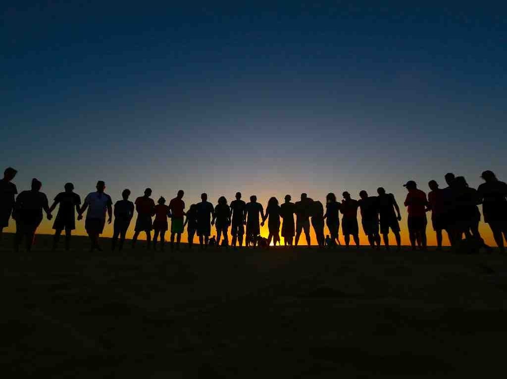 people who are united standing on the beach in front of the rising sun