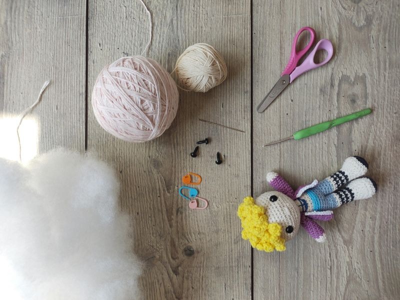 Crochet amigurumi kit with yarn, stuffing, hook, and a handmade doll on a wooden surface.