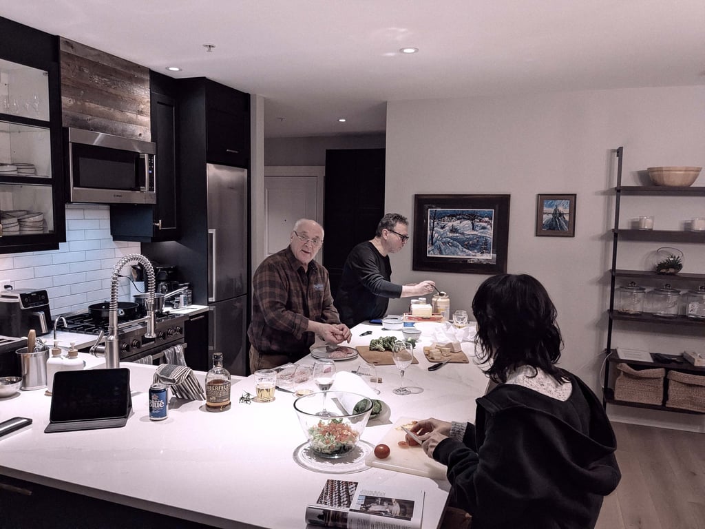Three people preparing food together in a home kitchen, working around a kitchen island with dishes.