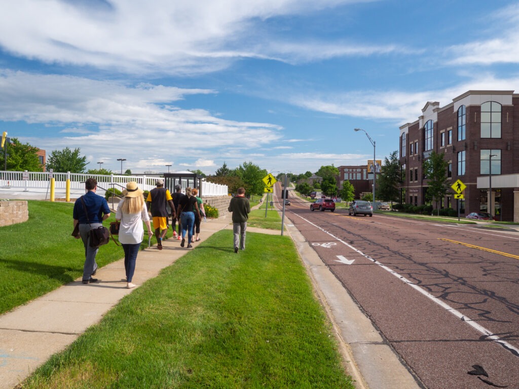 Crowd of people walking on a sidewalk next to a busy road