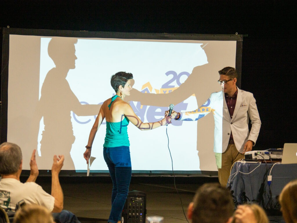 Two people exchanging a microphone in front of a screen
