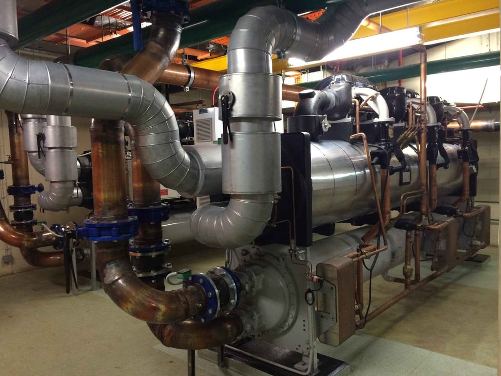 Industrial HVAC chiller system with insulated steel pipes and copper plumbing in a plant room.