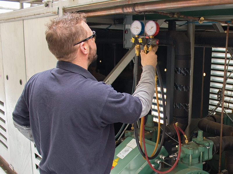 Professional HVAC technician using a manifold gauge set to check pressure on a commercial chiller unit.