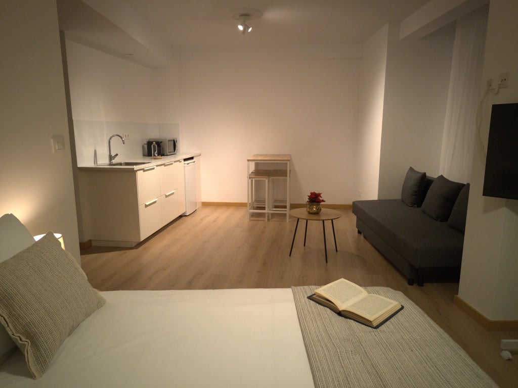 Habitación doble en Hotel Arias, Vigo, con salón, sofa, mesa y encimera, con un libro sobre la cama
