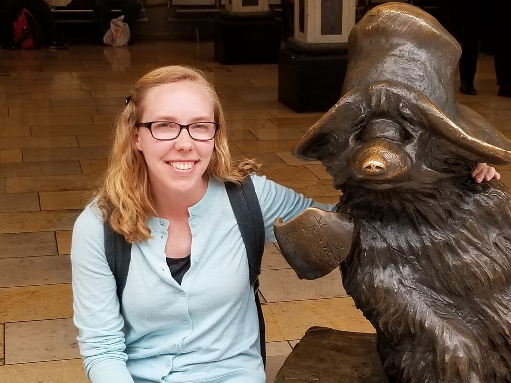 Sarah Schedler, editor for indie authors, poses for a photo next to a statue of Paddington Bear.