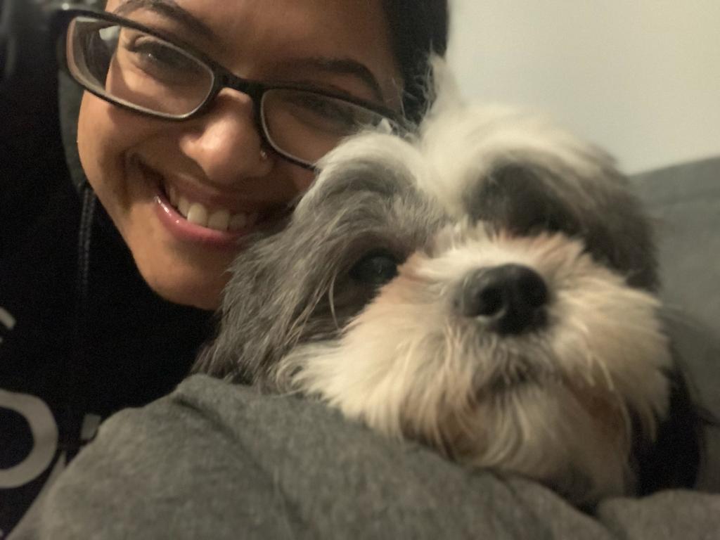 Local pet sitter smiling and cuddling small grey and white dog, a Shih Tzu cross Bichon