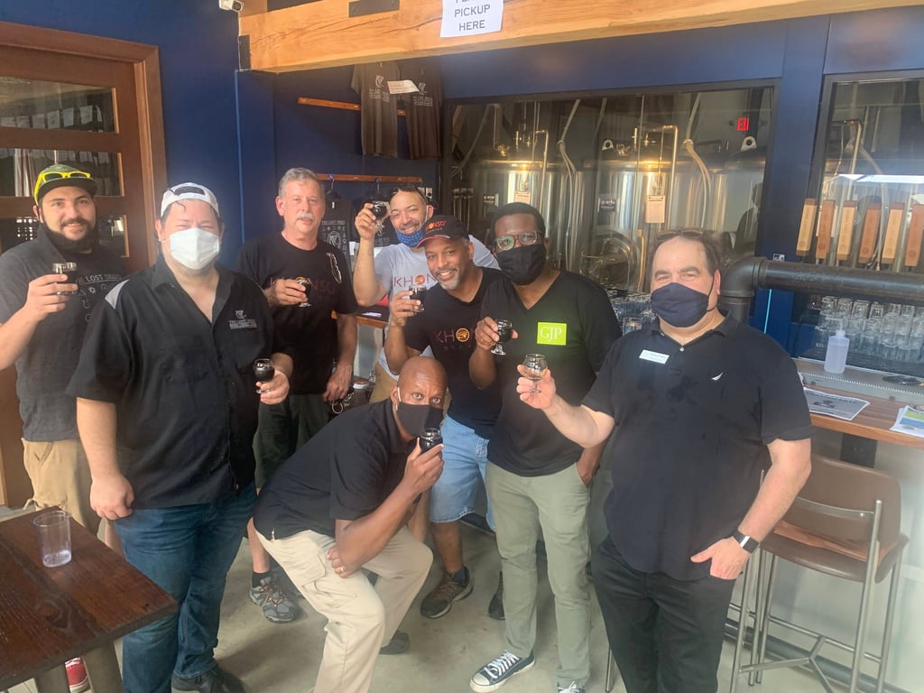 A diverse group of men wearing face masks enjoy a craft beer tasting at a local brewery taproom.