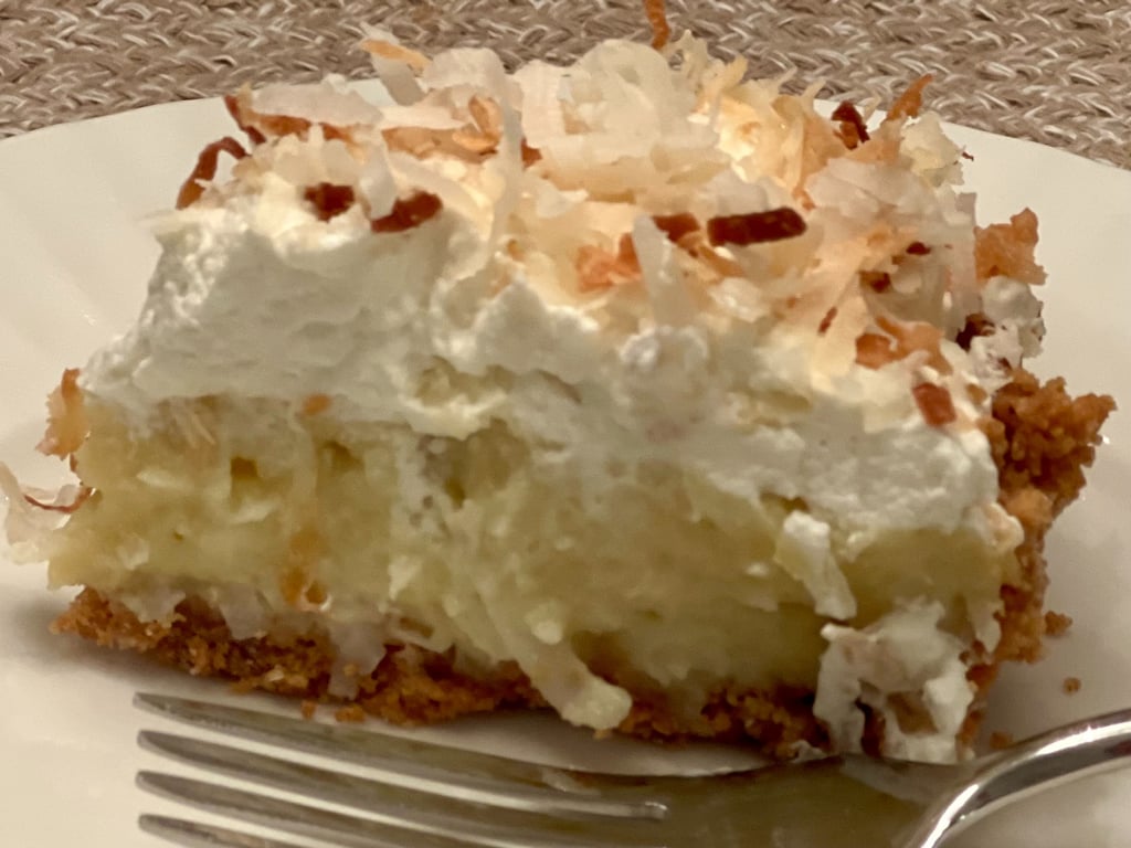A slice of homemade coconut cream pie with whipped cream and toasted coconut flakes.
