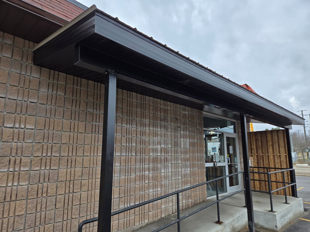 Commercial building exterior featuring a black metal awning, concrete block wall, and accessible entrance ramp.