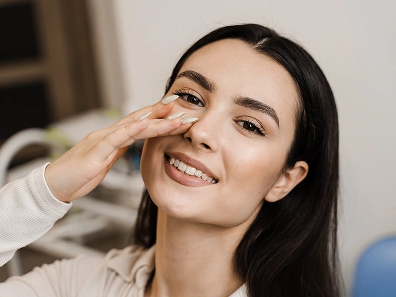 Smiling woman gently touches her nose, showing satisfaction.