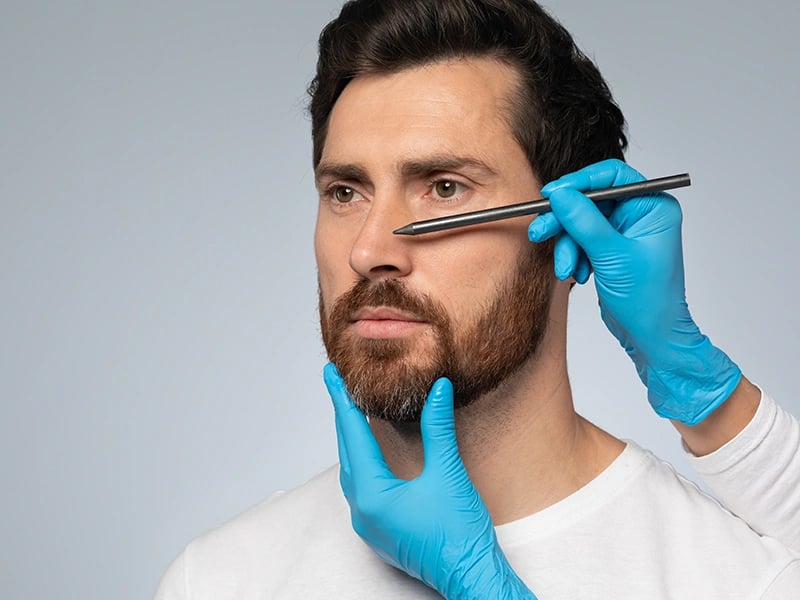 Wireframe nose on man's face, gloved hand touches, symbolizing surgical planning.
