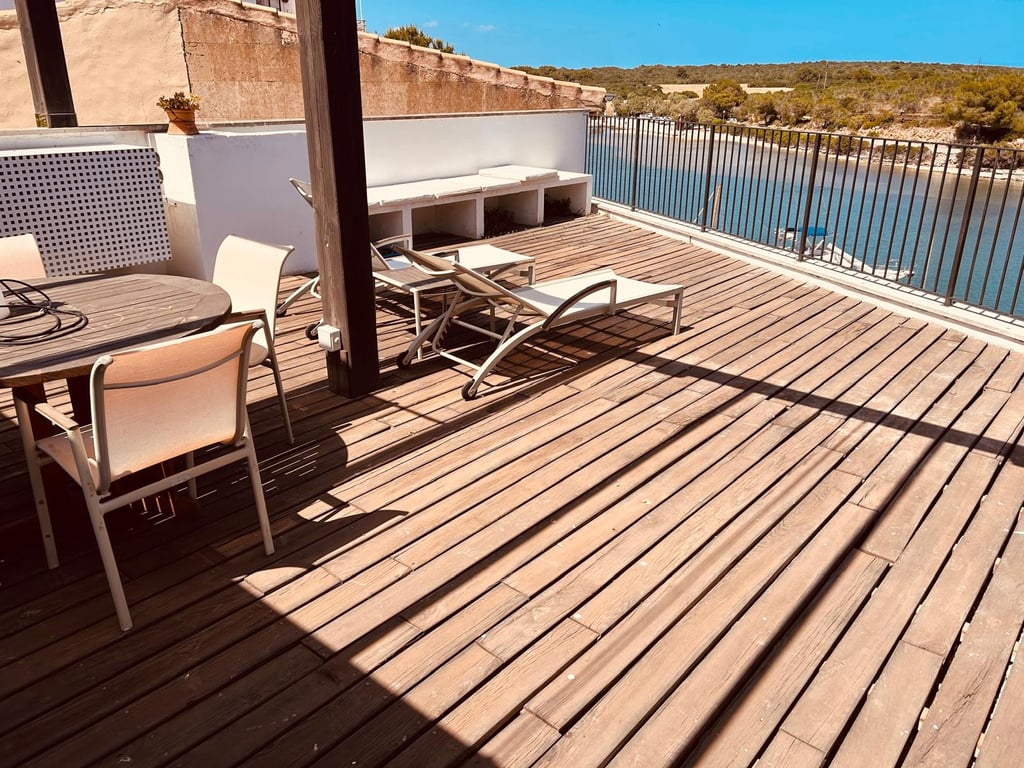 Luxury wooden deck terrace with lounge chairs and dining table overlooking a scenic river bay.