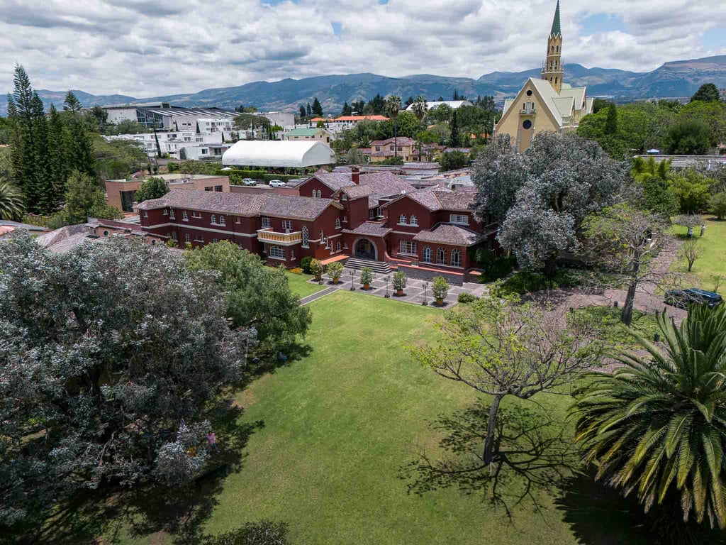 Fotografía aérea de gran casa religiosa de color rojo rodeada de hermoso jardín verde en Quito Ecuador