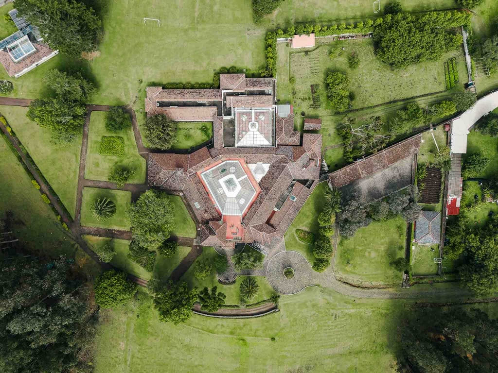 Fotografía con dron de mansión colonial de paredes blancas con techo naranja, cúpulas rodeada de naturaleza Quito Ecuador