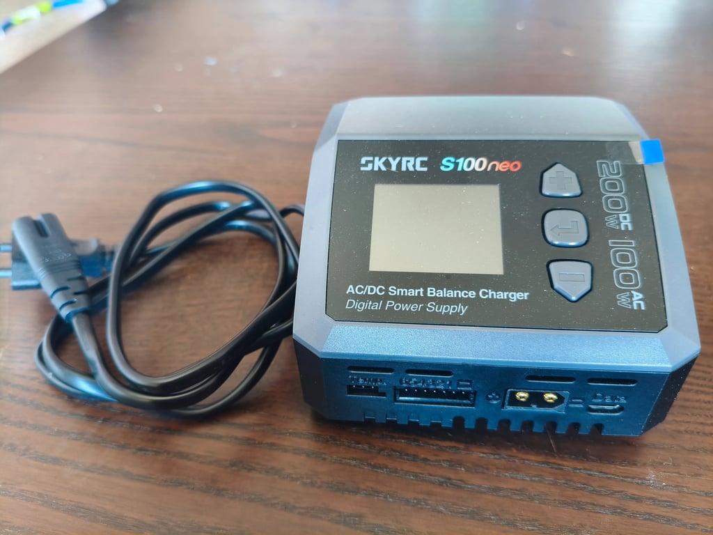 Carregador inteligente SkyRC S100neo AC DC completo com cabo de alimentação elétrica sobre mesa de m