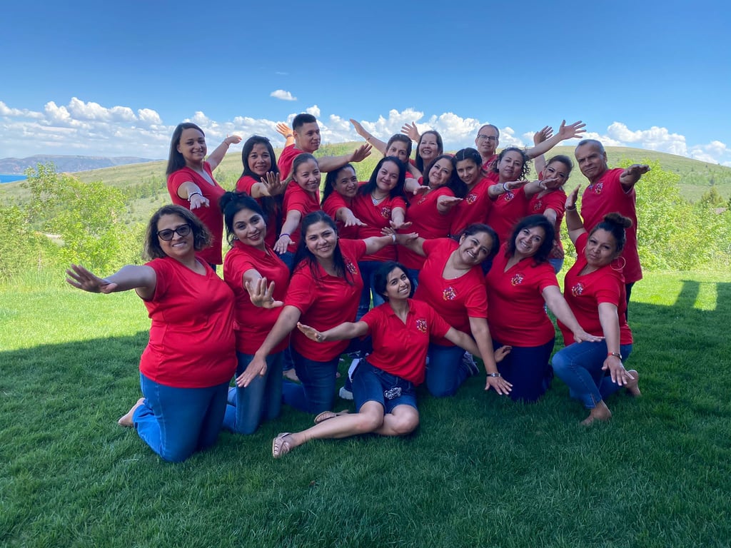 Diverse team of smiling colleagues wearing red shirts posing outdoors on a green lawn.