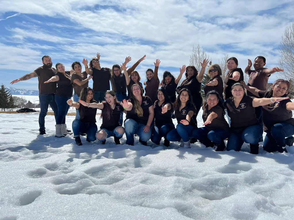 A diverse team in matching brown shirts posing together in the snow under a bright blue sky.