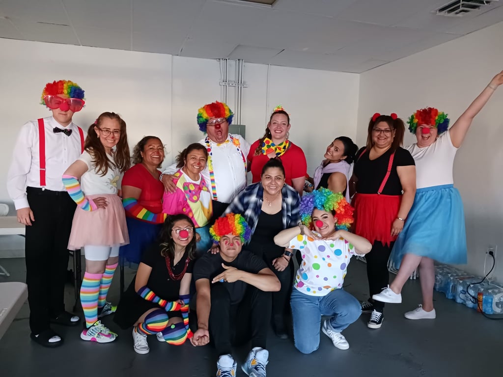 A diverse group of cheerful people wearing colorful clown wigs, costumes, and red noses for a party.