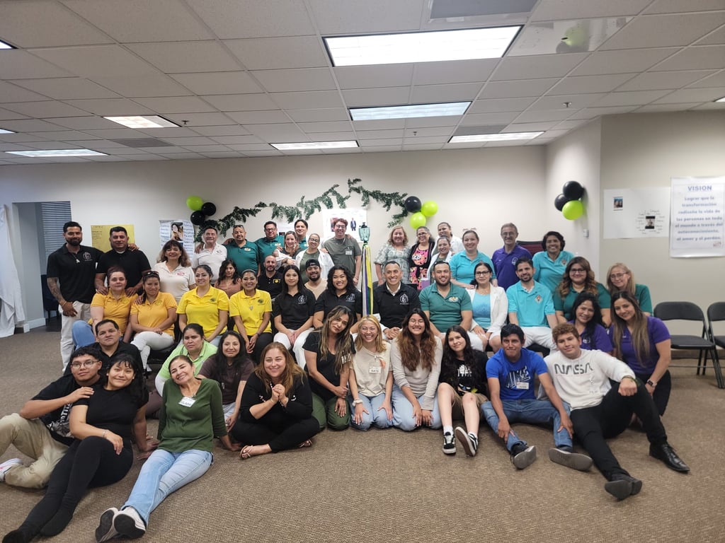 A large diverse group of community volunteers posing for a team photo in a brightly lit indoor meeting room.