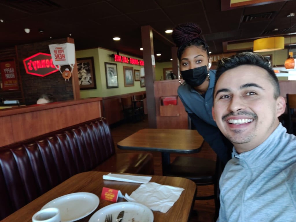 A happy customer takes a selfie with a waitress wearing a mask inside a Denny's restaurant.
