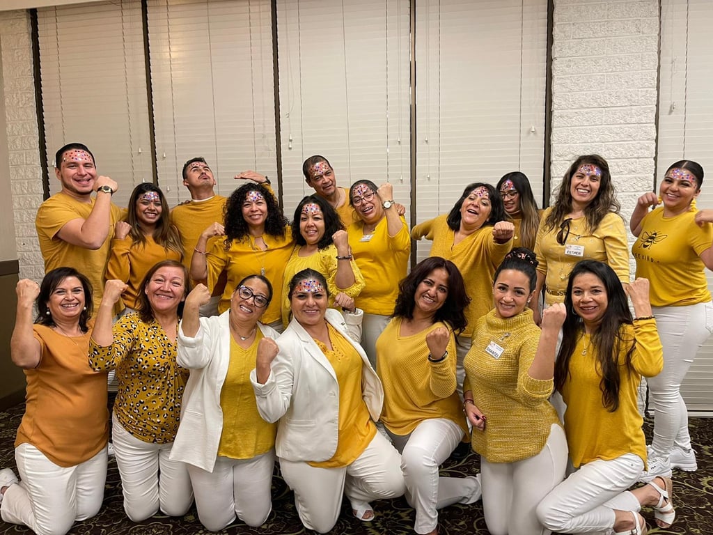 A diverse group of coworkers in yellow shirts and white pants pose for a corporate team building photo.
