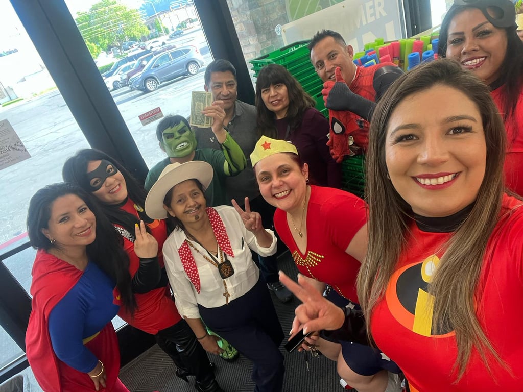 A group of smiling employees wearing superhero costumes for a retail store event or Halloween party.