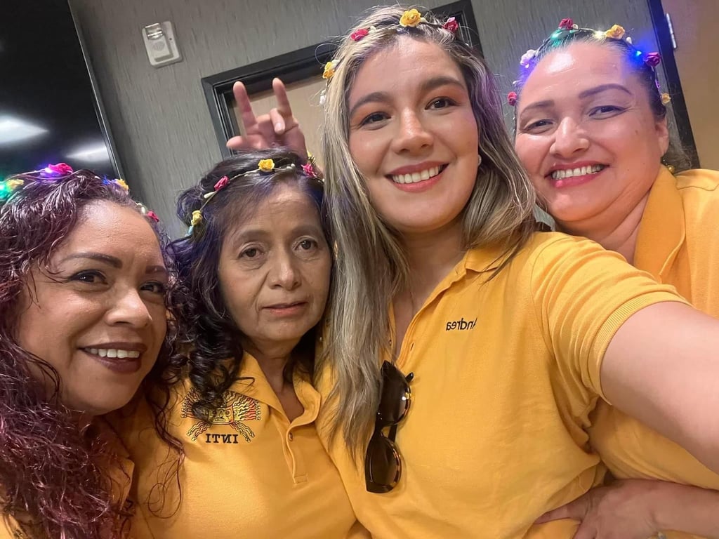 Four smiling women in yellow polo shirts wearing colorful floral crowns with LED lights.