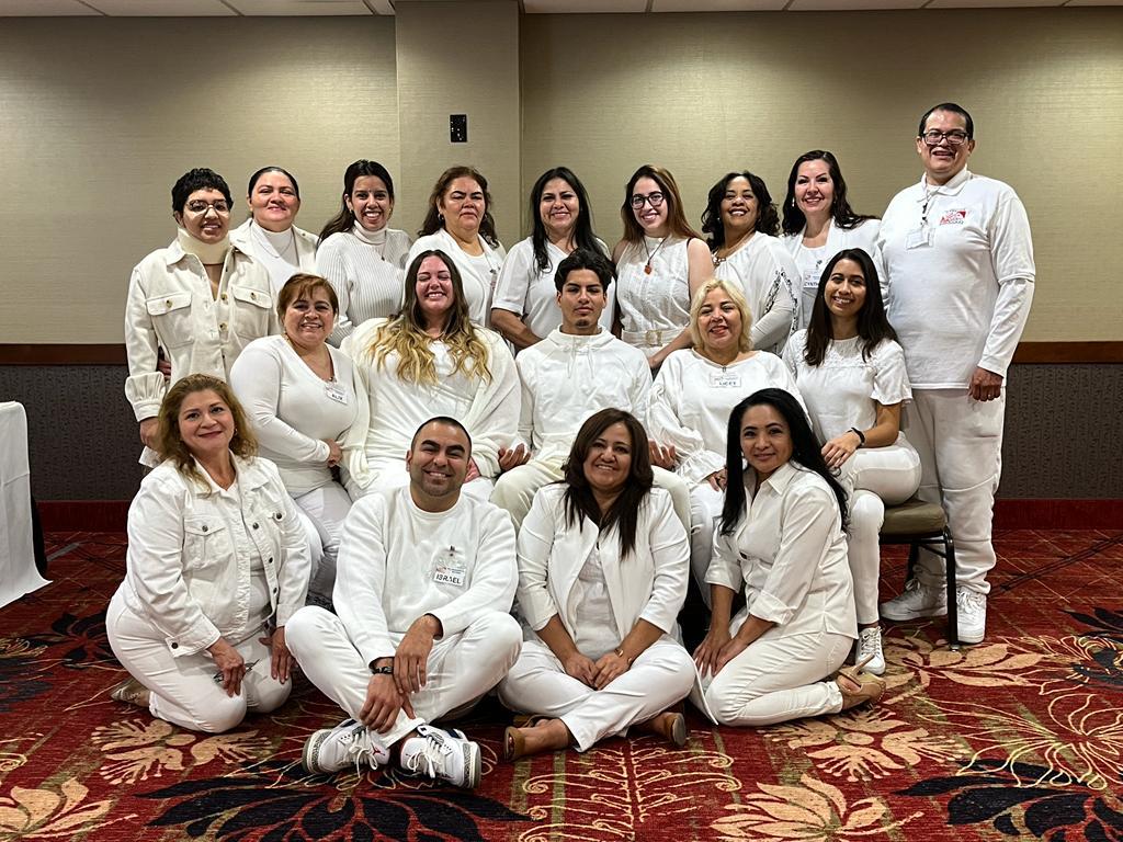 Diverse group of smiling people in white professional attire posing for a team photo in a conference room.