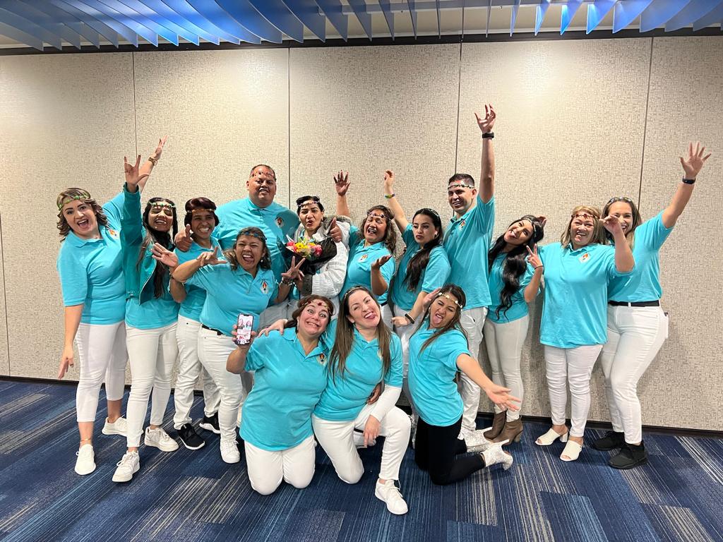 A cheerful group of people in matching turquoise polo shirts and white pants posing for a team photo.